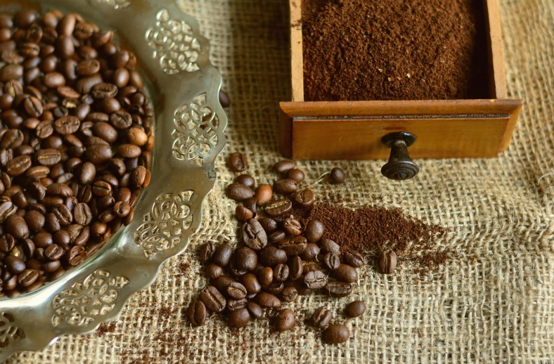 a bowl of coffee beans next to a box of coffee beans, a portrait, by Virginia Lee Burton, featured on pixabay, renaissance, powder, fine texture detail, dust around, burnt umber and blue