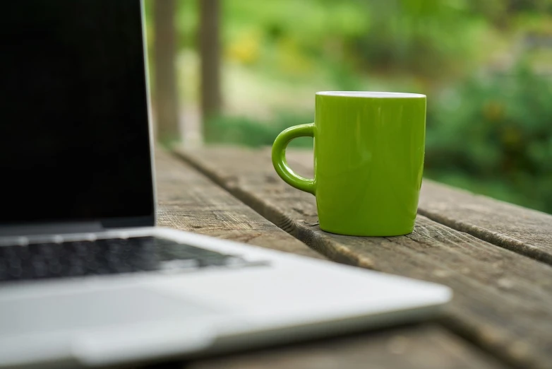 a green mug sitting on top of a wooden table next to a laptop computer, a picture, green terrace, lush green, technologies, photo - shot