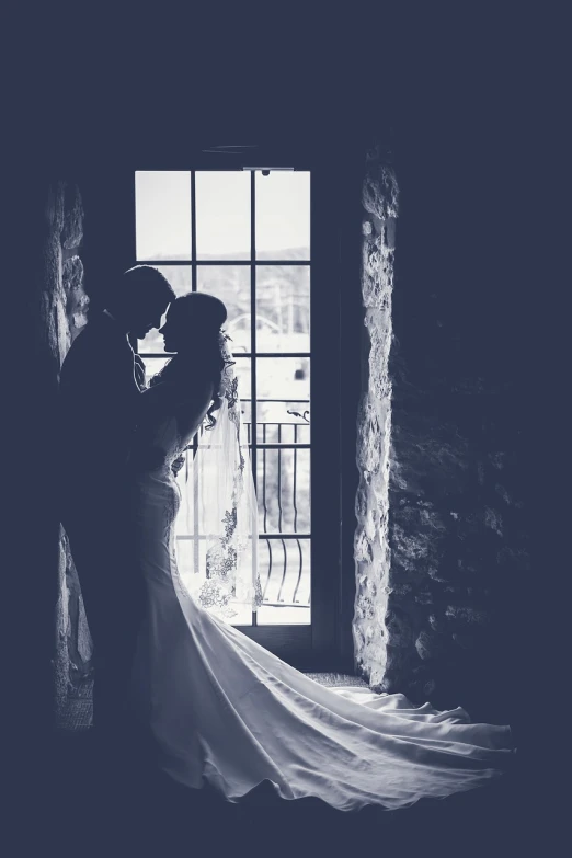 a bride and groom kissing in front of a window, a black and white photo, romanticism, stylized silhouette, located in a castle, deep lighting, monochrome color