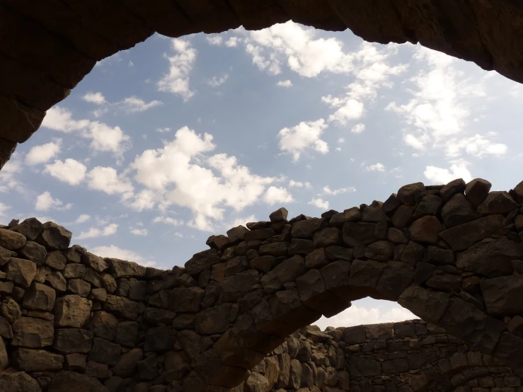 a stone arch with a sky in the background, a picture, by Steven Belledin, nubian, old stone wall, looking at the ceiling, light and clouds