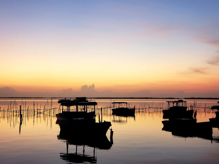 a group of boats floating on top of a lake, by Odhise Paskali, shutterstock, minimalism, vibrant sunrise, phuoc quan, peaceful evening harbor, silhouetted