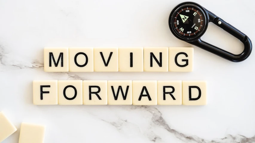 the word moving forward spelled in scrabbles next to a compass, happening, forward facing pose, 🔞🤡, 🚿🗝📝