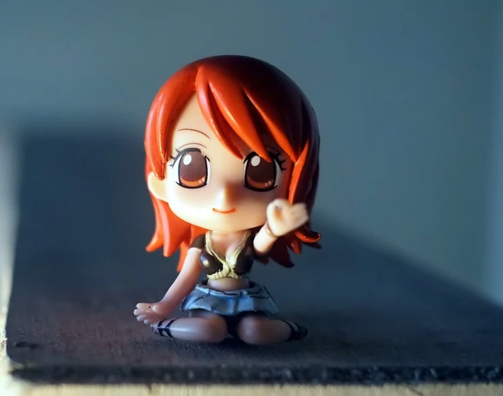 a small figurine of a girl sitting on a table, a picture, pixiv, nami from one piece, portrait mode photo, waving at the camera, closeup!!!!!!
