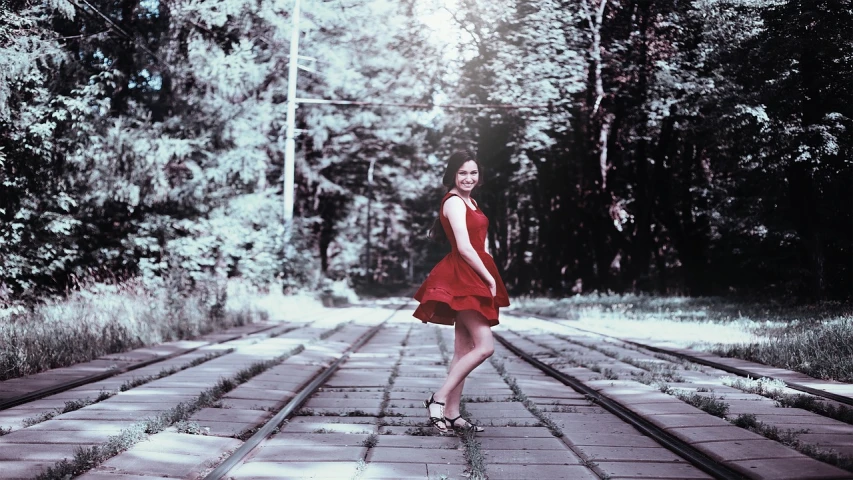 a woman in a red dress standing on a train track, inspired by Alexander Deyneka, art photography, against the backdrop of trees, low quality photograph, smooth in _ the background, desaturated