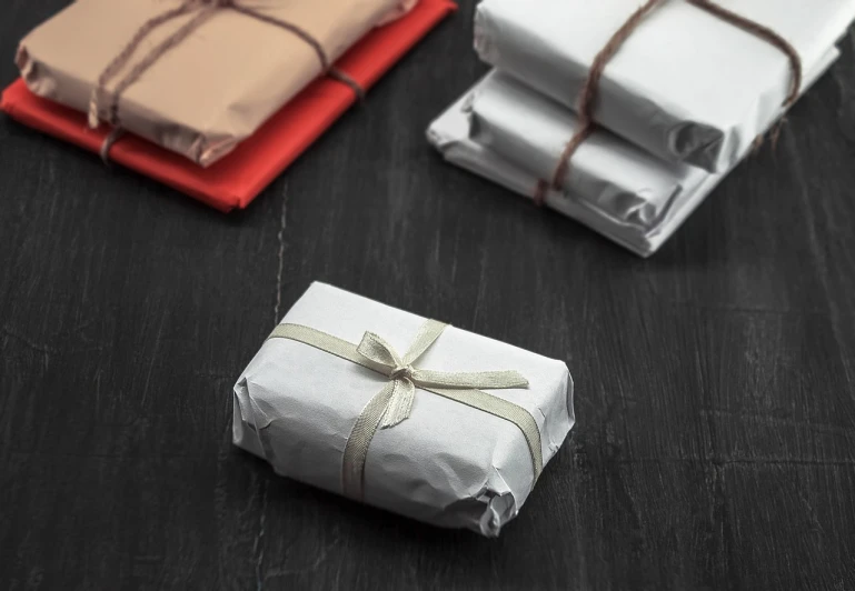 a stack of wrapped presents sitting on top of a wooden table, by david rubín, shutterstock, bauhaus, charcoal and silver color scheme, delivering mail, miniature product photo, stock photo