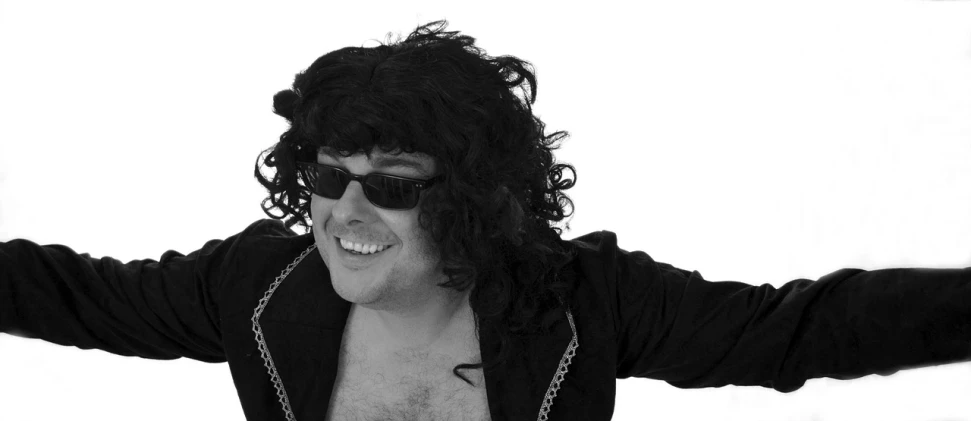 a black and white photo of a man with a chain around his neck, an album cover, inspired by Tom Bonson, realism, funny sunglasses, wig, fancy dress, shoulder-length black hair