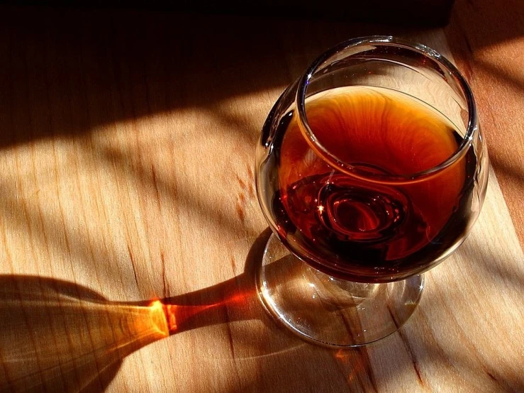 a glass of wine sitting on top of a wooden table, by Adam Chmielowski, pixabay, maple syrup highlights, great light and shadows”, shot on a 2 0 0 3 camera, deep colours. ”