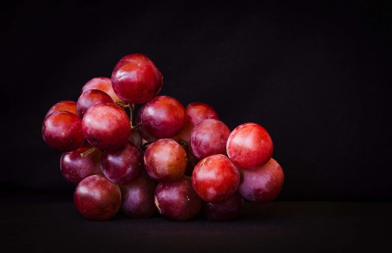 a bunch of red grapes sitting on top of a table, by Thomas Häfner, unsplash, hyperrealism, with a black background, medium format. soft light, high quality product image”