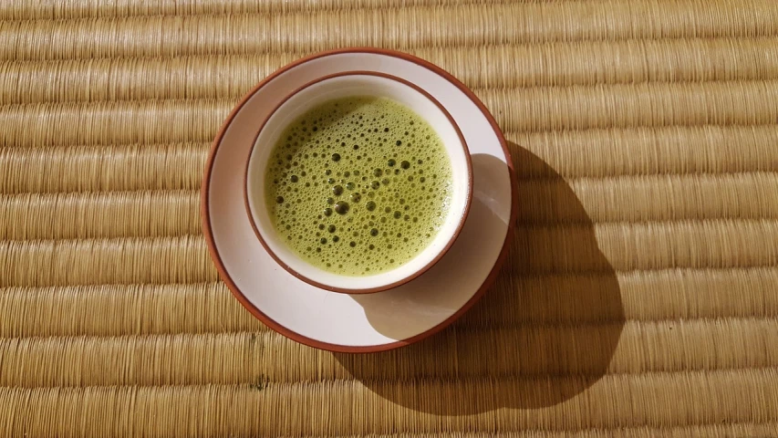 a cup of green tea sitting on top of a wooden table, a picture, flickr, sōsaku hanga, powder, photo taken in 2018, glazed, very tasty