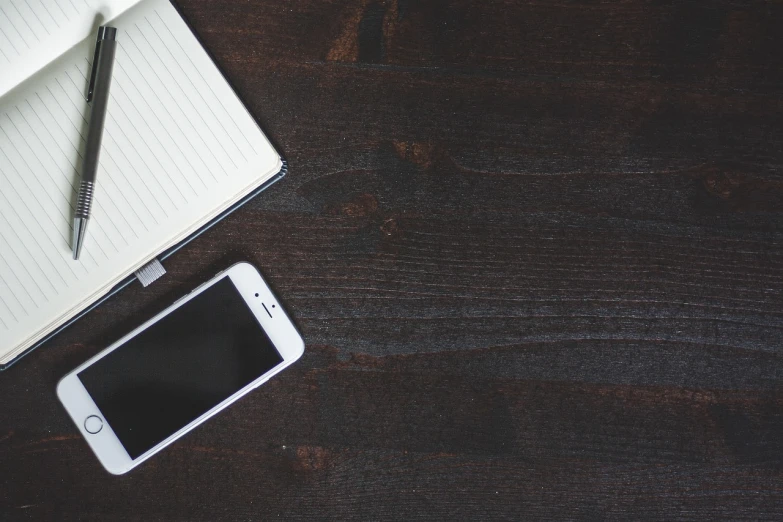 a cell phone sitting on top of a wooden table, by Robbie Trevino, pexels, writing in journal, banner, dark-skinned, white space in middle