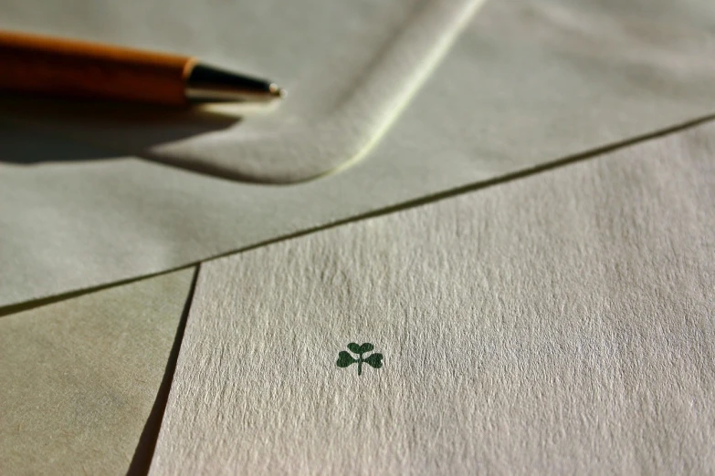 a pen sitting on top of a piece of paper, a macro photograph, inspired by Masamitsu Ōta, letterism, four leaf clover, simple elegant design, cards, celtic symbols
