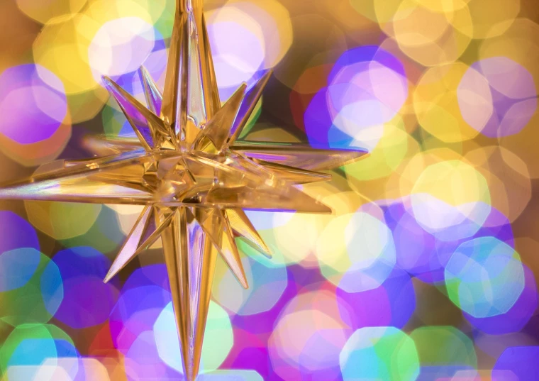 a gold star ornament hanging from a christmas tree, a photo, inspired by Rudolph F. Ingerle, pexels, colorful refracted sparkles, purple and yellow lighting, christian saint, kaleidoscope