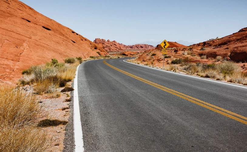 a yellow street sign sitting on the side of a road, a photo, by Whitney Sherman, shutterstock, bright red desert sands, many smooth curves, usa-sep 20, stony road