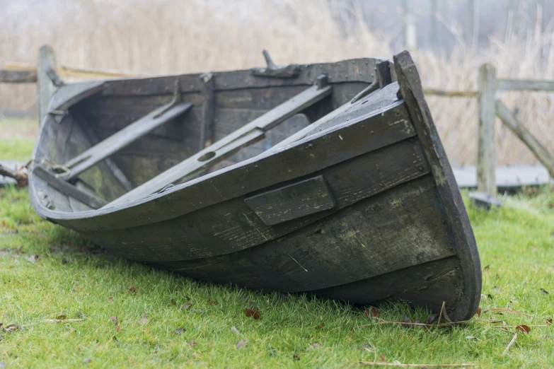 a wooden boat sitting on top of a lush green field, a picture, by Richard Carline, shutterstock, photo of poor condition, low dutch angle, dark dingy, close up shot from the side