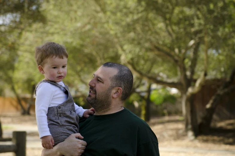 a man holding a small child in his arms, a portrait, by Matt Cavotta, trees in the background, napa, greg rutkowski and carvaggio, programming