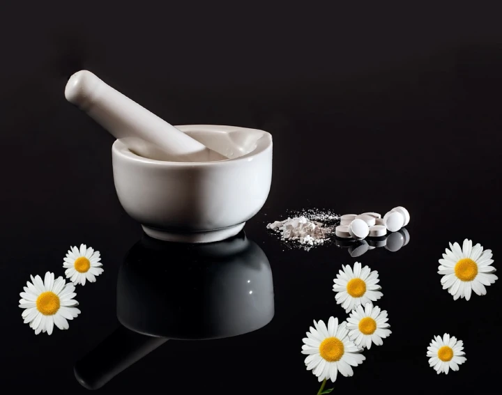 a mortar and some white flowers on a black surface, a still life, by Rhea Carmi, pixabay, pharmacy, lying on a bed of daisies, bowl, salt