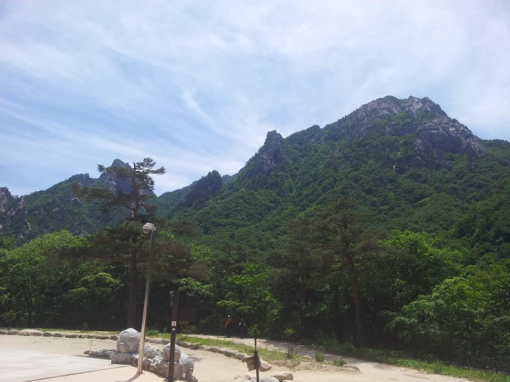 a motorcycle parked on the side of a road in front of a mountain, inspired by Kim Myeong-guk, hideen village in the forest, сastle on the rock, sangyeob park, solo hiking in mountains trees