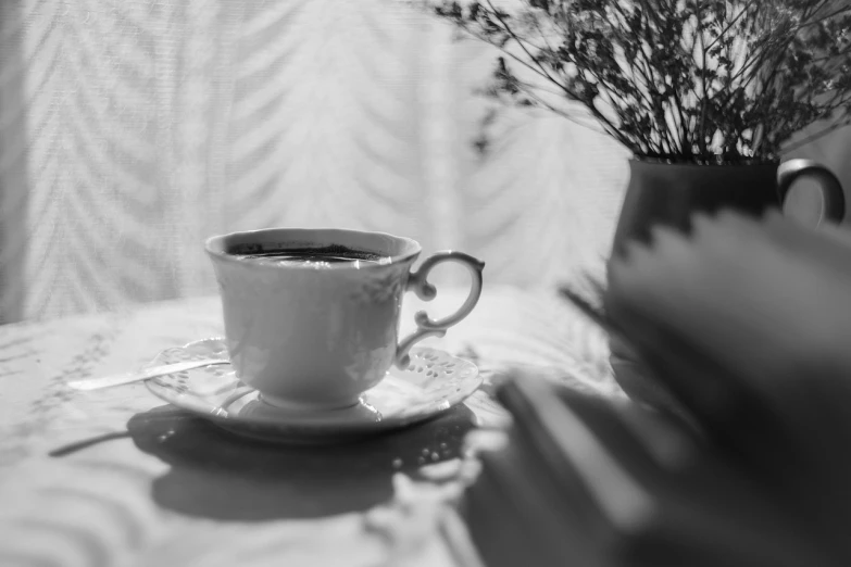 a cup of coffee sitting on top of a saucer, a black and white photo, romanticism, sun dappled, books and flowers, close up portrait photo, bright daylight indoor photo