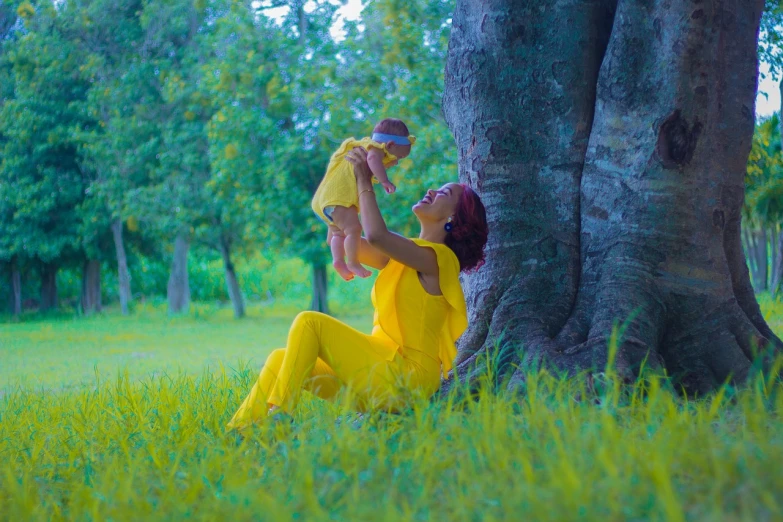 a woman holding a baby up to a tree, inspired by Anne Geddes, pexels, art photography, lady using yellow dress, stock footage, innocent look. rich vivid colors, ukraine. professional photo