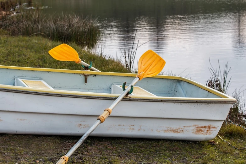 a row boat sitting on top of a grass covered field, a photo, by Richard Carline, shutterstock, two crutches near bench, white and yellow scheme, medium close up shot, boats in the water