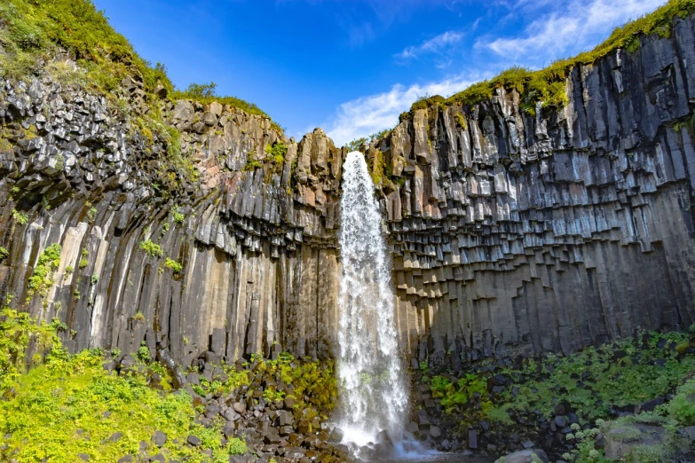 a waterfall in the middle of a lush green forest, by Þórarinn B. Þorláksson, shutterstock, hurufiyya, tessellated planes of rock, tall obsidian architecture, stock photo, high detailed thin stalagtites