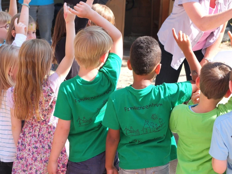 a group of children standing next to each other, a photo, by Christen Dalsgaard, pixabay, green shirt, waving arms, performance, close-up shot from behind