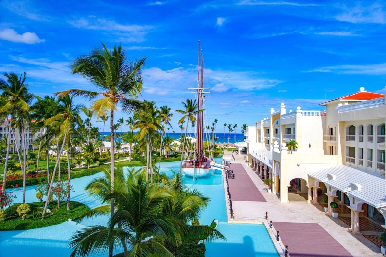 a resort with a swimming pool surrounded by palm trees, a stock photo, by Alexander Robertson, shutterstock, sail boat on the background, wide high angle view, theron, ultra wide lens shot