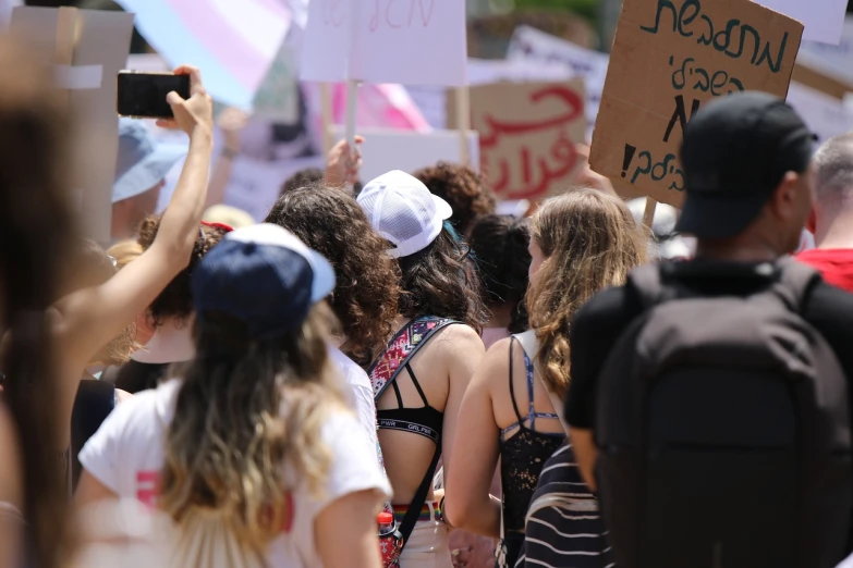 a group of people holding up signs at a protest, a photo, by Alexis Grimou, shutterstock, woman holding another woman, israel, white and pink, with his back turned