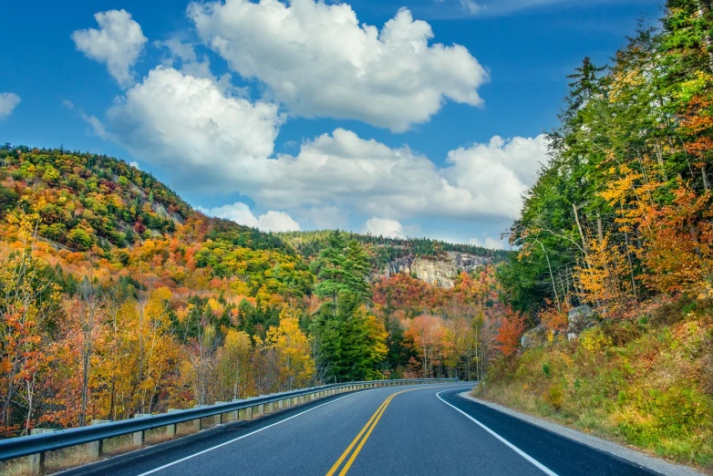 an empty road with a mountain in the background, by Thomas M. Baxa, shutterstock, hudson river school, vermont fall colors, trees and cliffs, full of colorful vegetation, car on highway