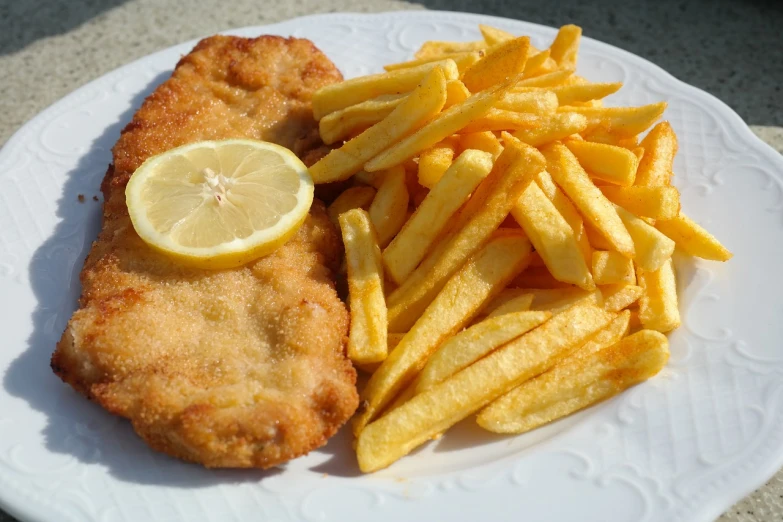a white plate topped with french fries and a lemon slice, inspired by Chippy, renaissance, radoslav svrzikapa, sunny day, fish, jugendstill