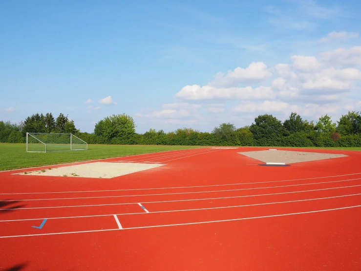 a red track with a soccer field in the background, a picture, by Anna Haifisch, shutterstock, well edited, gigantic landing pad, eldenring, hard clay