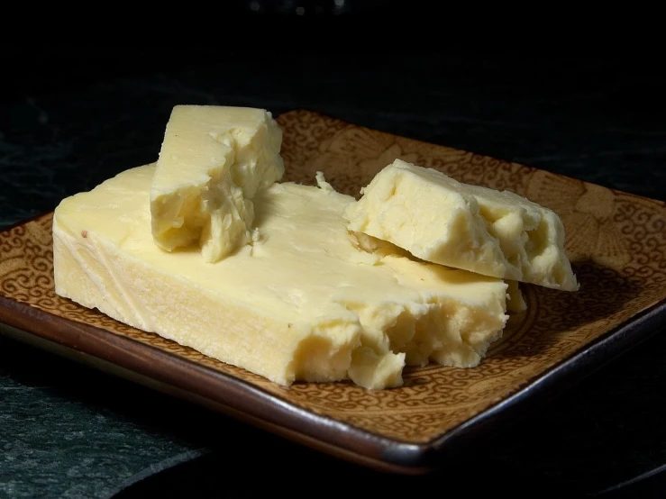 a piece of butter sitting on top of a brown plate, by John Murdoch, flickr, cheeses, pale white skin, bolero, highly textured