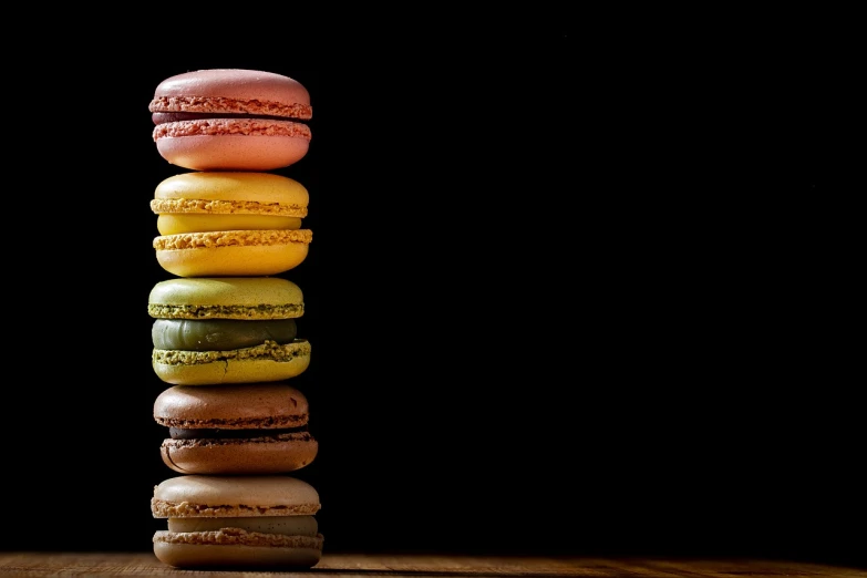 a stack of macarons sitting on top of a wooden table, by Dietmar Damerau, bright on black, in a row, towering, different colors