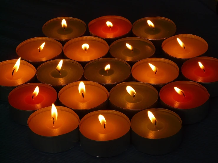 a group of lit candles sitting on top of a table, a picture, pixabay, dark grey and orange colours, bottom angle, multi - coloured, pyromallis rene maritte
