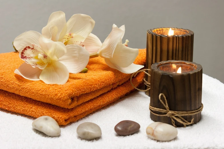 a towel sitting on top of a table next to a candle, stones, orange and white color scheme, setting is bliss wallpaper, beautiful image