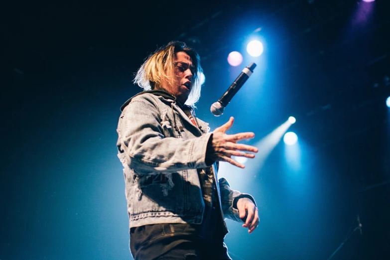 a man standing on top of a stage holding a microphone, a portrait, by Jan Tengnagel, unsplash, jamie campbell bower, trippie redd, till lindemann, looking left