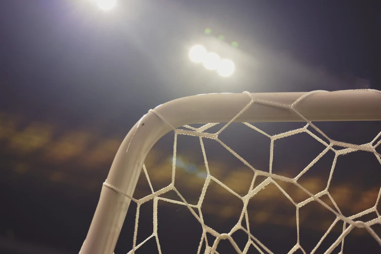 a close up of a soccer net with lights in the background, a picture, by Christen Dalsgaard, shutterstock, brine lacrosse stick, seen from below, 35 mm product photo”, beautiful rim lighting