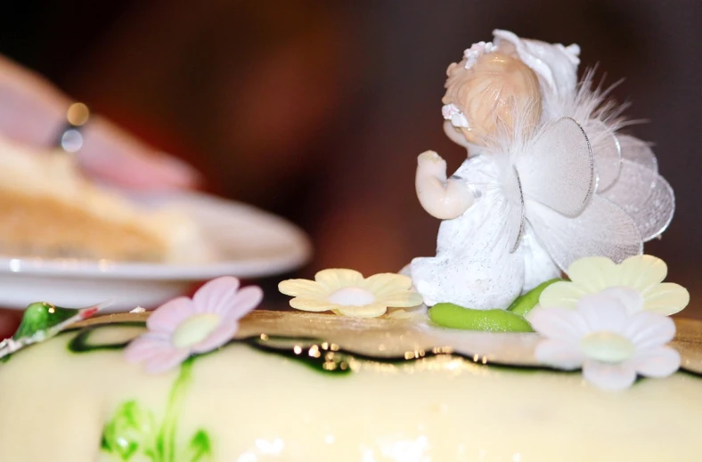 a small angel figurine sitting on top of a cake, a picture, by Marie Angel, pixabay, zoomed in shots, decorated with flowers, closeup at the food, wide angle”