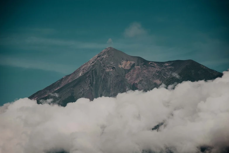 a mountain covered in clouds under a blue sky, a picture, sumatraism, complex and desaturated, mount fuji background, irish mountains background, cone