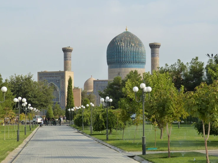 a walkway in the middle of a park with a mosque in the background, inspired by Kamāl ud-Dīn Behzād, samarkand, view from the street, the empress’ swirling gardens, taken in the late 2010s