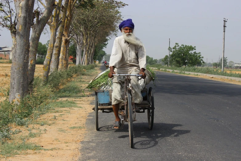 a man riding a bike with a basket on the back of it, a picture, by Robert Brackman, flickr, samikshavad, long white beard, long highway, posing for camera, 2 0 7 7