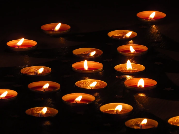a group of lit candles sitting on top of a table, a picture, pexels, hurufiyya, stock photo, warm volumetric lights, on a black background, panels