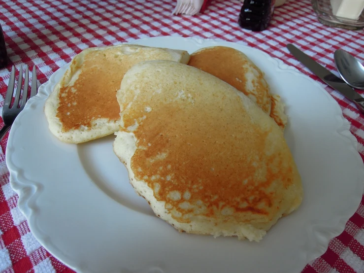 a white plate topped with pancakes on top of a red and white checkered table cloth, by Edna Mann, flickr, soft and fluffy, bread, poker, closeup - view