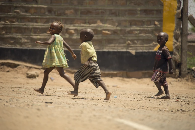 a group of children walking across a dirt field, a picture, by Adam Manyoki, afp, toddler, raising between the buildings, girl running