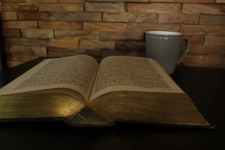 an open book sitting on top of a table next to a cup of coffee, a picture, old testament, no words 4 k, gold, full body shot