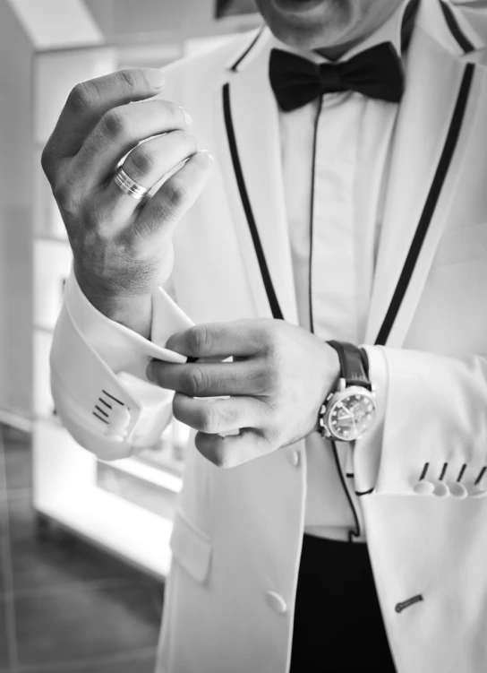 a black and white photo of a man in a tuxedo, a black and white photo, pexels, detailed jewelry, white sleeves, details and vivid colors, white clothes