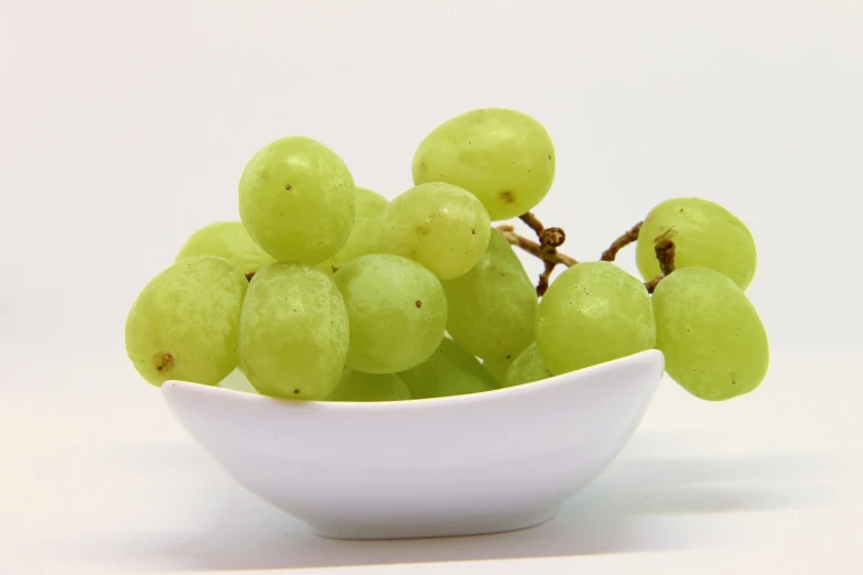a white bowl filled with green grapes on top of a table, pixabay, bauhaus, white backround, amber, pure white, jenny seville