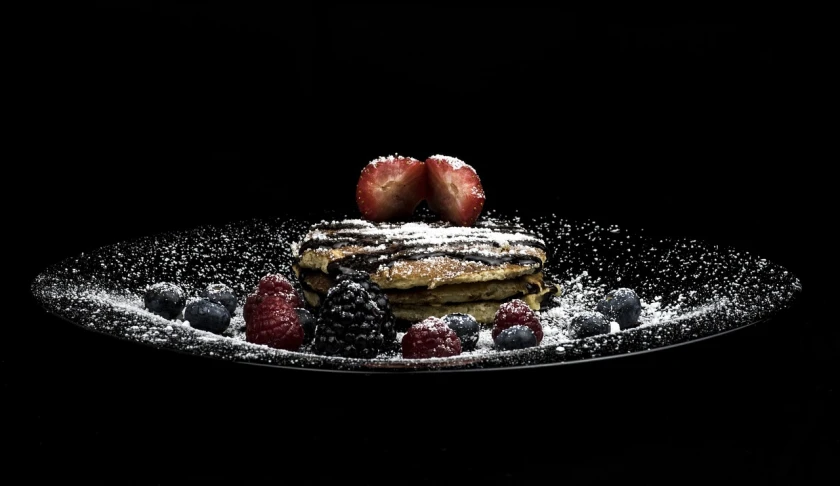 a plate topped with a stack of pancakes covered in powdered sugar, by Etienne Delessert, pexels, romanticism, berries dripping, with a black background, high contrast hyperrealism 8k, backlighted