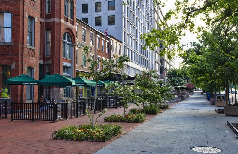 a sidewalk lined with tables and umbrellas next to tall buildings, a photo, by Dennis Flanders, shutterstock, plein air, capitol hill, ivy's, landscape architecture photo, sparsely populated