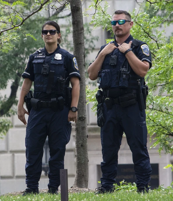 two police officers standing next to a tree, a photo, dc, usa-sep 20, tactical vests and holsters, fascist police